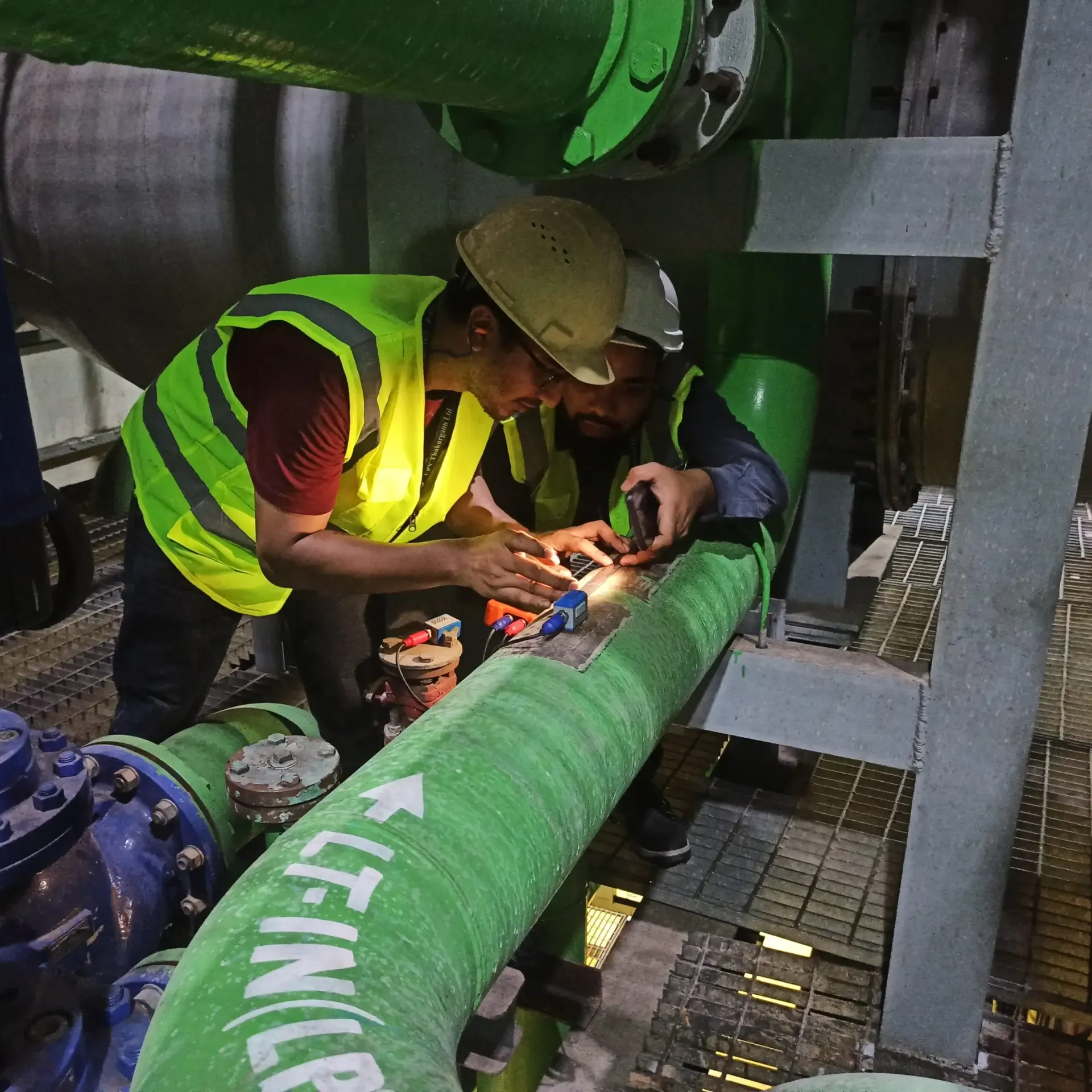 Two engineers taking measurements on a green steam pipe