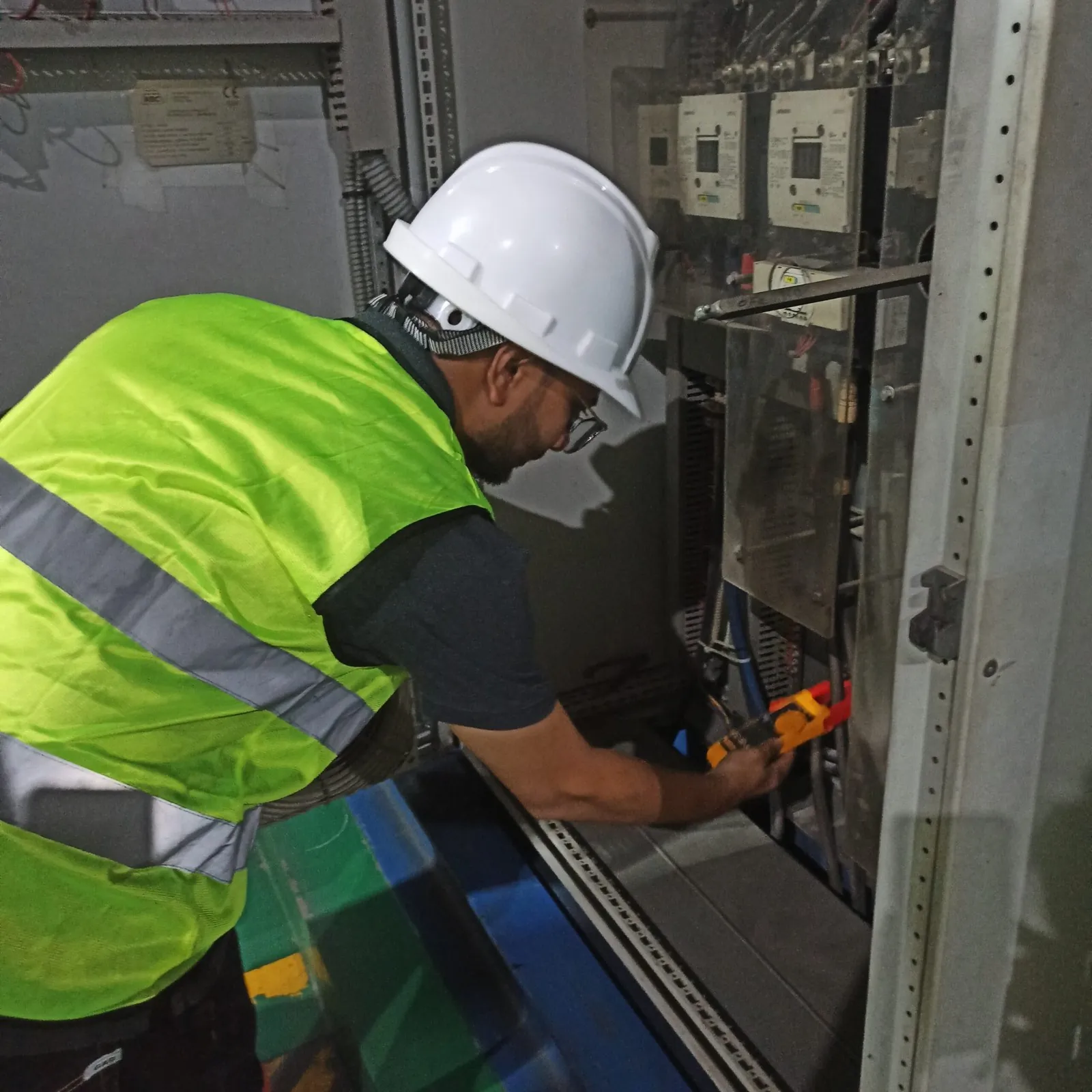 Engineer in a hard hat measuring at an electrical panel