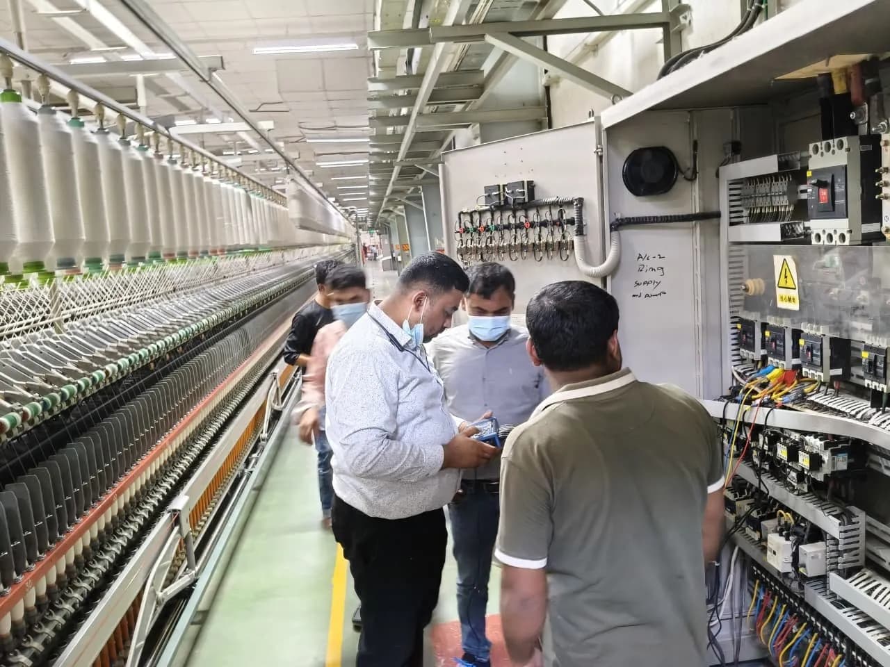 Engineers and plant staff at a control panel beside a spinning machine